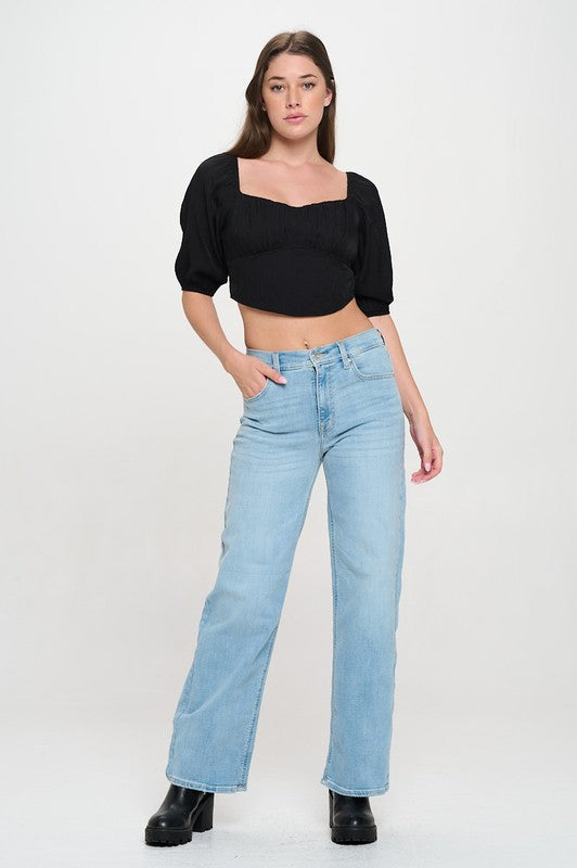 Woman wearing a off-shoulder top with white pants on a light gray background
