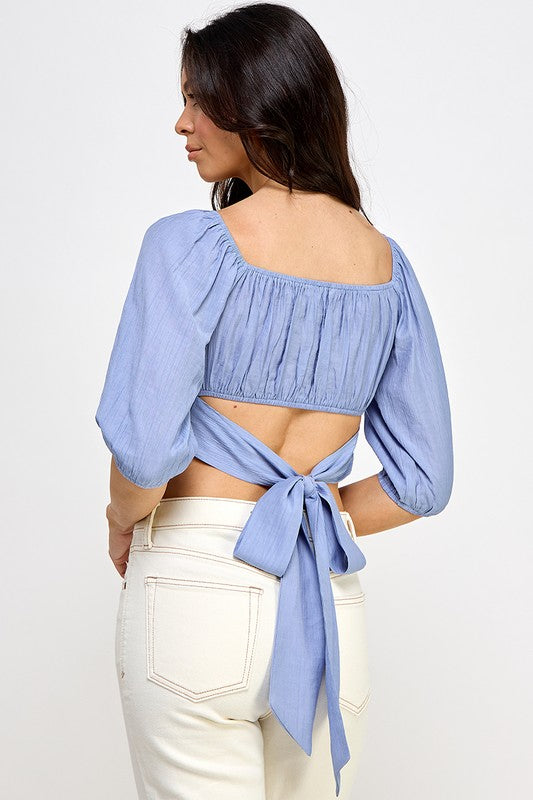 Woman wearing a off-shoulder top with white pants on a light gray background