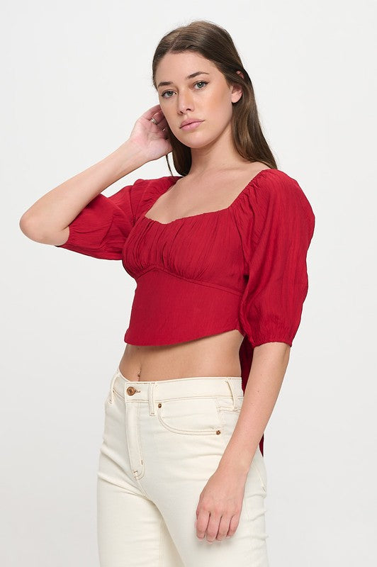 Woman wearing a off-shoulder top with white pants on a light gray background