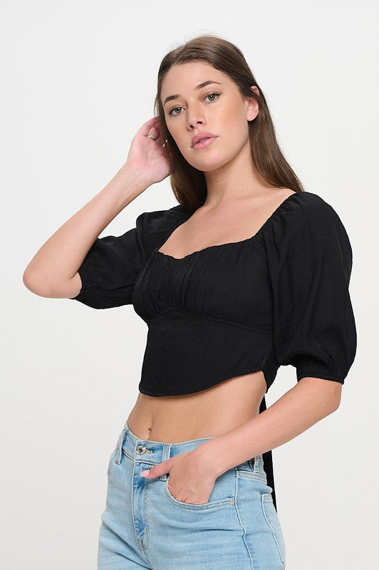 Woman wearing a off-shoulder top with white pants on a light gray background