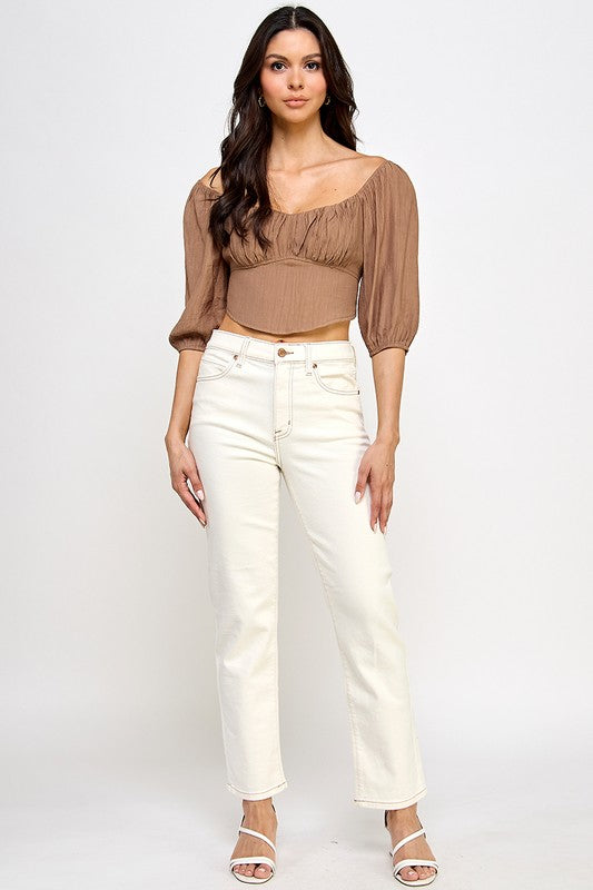 Woman wearing a off-shoulder top with white pants on a light gray background