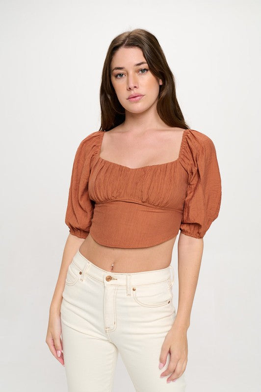 Woman wearing a off-shoulder top with white pants on a light gray background