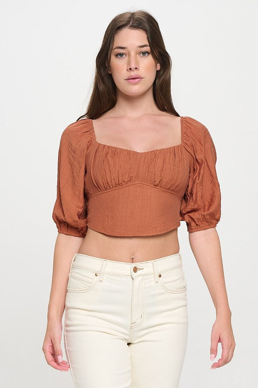 Woman wearing a off-shoulder top with white pants on a light gray background