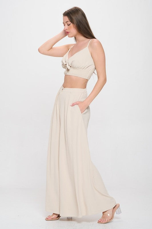 Woman wearing a beige top and white pants on a white background