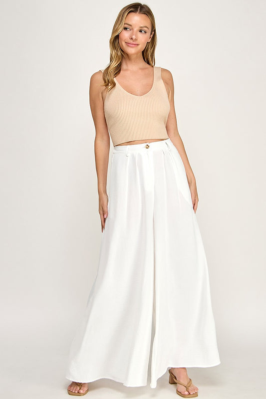 Woman wearing a beige top and white pants on a white background