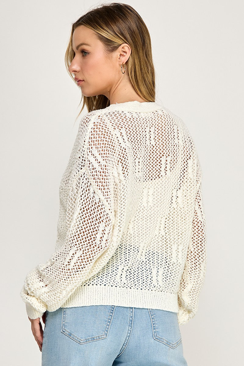 A woman models the SW5690 V-neckline, button-front long sleeves open-knit cardigan with a see-through pattern and light blue jeans, standing with her back and side to the camera—ideal for effortless transitional style.