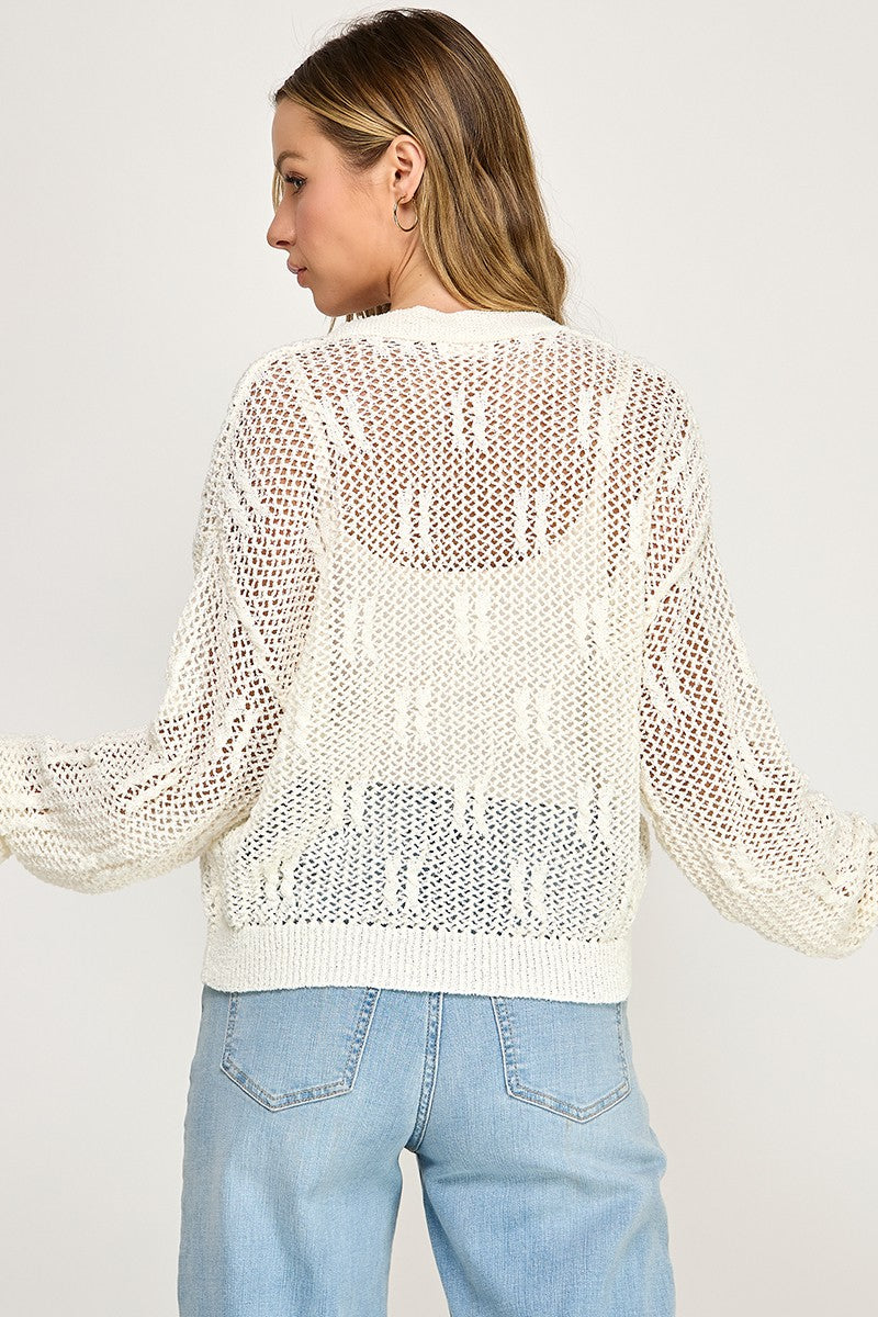 A woman faces away, wearing the SW5690 V-neckline button-front long sleeves open-knit cardigan over a white top and light blue jeans against a plain background—embodying effortless transitional style.